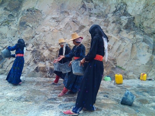 Women sprinkle water to moisten the concrete on a new road in Al Gafariyah distric