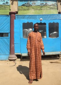 un jeune homme bénéficiaire du soutien d’ACTED devant son stand de chaussures sur un marché local de la capitale