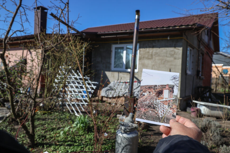 Nataliia holds up a photo of their home after it was destroyed by a missile. In the background, the newly renovated house stands as a symbol of resilience.